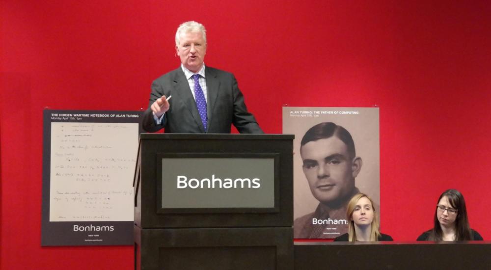مدير صالة بونهامز بنيويورك أثناء المزاد وخلفه صورة آلان تورنغ