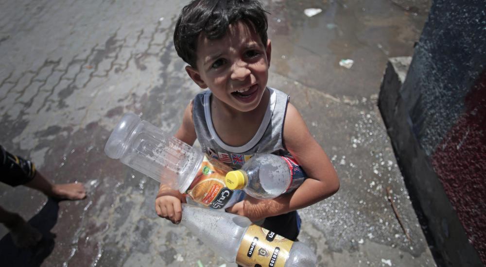 طفل فلسطيني يحمل زجاجات فارغة ليملأها بالمياه بسبب أزمة مياه الشرب