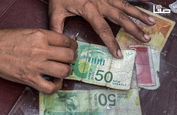 سيدة تُصلح أوراقًا مالية مهترئة في ظل نقص السيولة النقدية وتدفق الأموال من وإلى قطاع غزة